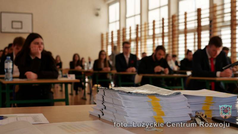 maturzyści podczas pisemnego egzaminu z języka polskiego, na pierwszym planie arkusze egzaminacyjne